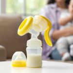 Breast pump on table against mother with baby at home, closeup